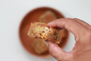 a close up of fried stuffed tofu or Gorengan Tahu Isi holding in hand isolated on white background and bowl of stuffed fried tofu blurry. Indonesian food concept.