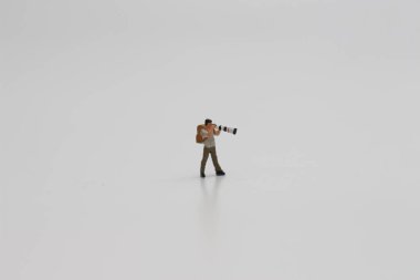 a close up of a miniature figure of a photographer with a camera and telephoto lens isolated on a white background. Miniature figure photo concept.