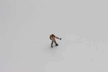 a close up of a miniature figure of a photographer with a camera and telephoto lens isolated on a white background. Miniature figure photo concept.