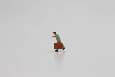 a close up of a miniature figure of an office worker carrying a suitcase isolated on a white background. Miniature figure photo concept.