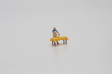 a close up of a miniature figure of a woman serving food on a table isolated on a white background. Miniature figure photo concept.
