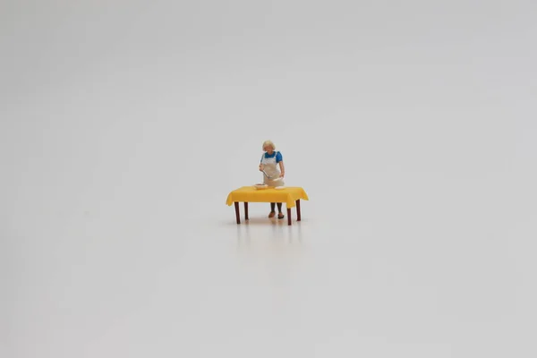 a close up of a miniature figure of a woman serving food on a table isolated on a white background. Miniature figure photo concept.