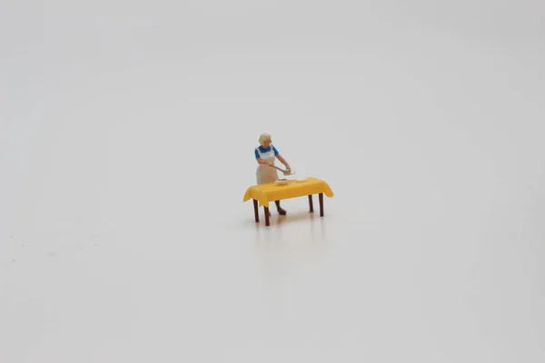a close up of a miniature figure of a woman serving food on a table isolated on a white background. Miniature figure photo concept.