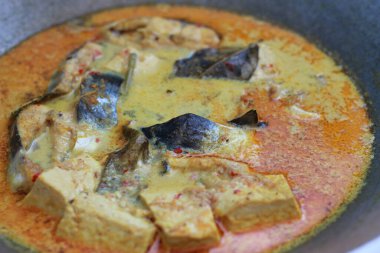 photo of tuna fish and white tofu in yellow spice sauce on a frying pan. Indonesian traditional food photo concept.