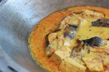 photo of tuna fish and white tofu in yellow spice sauce on a frying pan. Indonesian traditional food photo concept.
