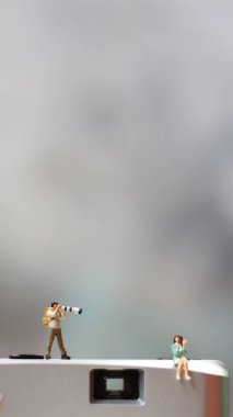 a miniature figure taking picture with a camera against a real camera in the background.