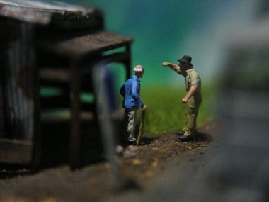 a close up of a miniature figure of an old man talking to other people in an old building by the side of the road.