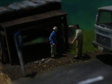 a close up of a miniature figure of an old man talking to other people in an old building by the side of the road.