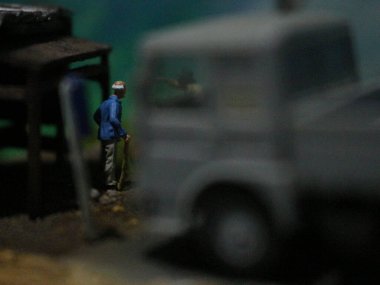 a close up of a miniature figure of an old man talking to other people in an old building by the side of the road.
