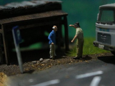 a close up of a miniature figure of an old man talking to other people in an old building by the side of the road.