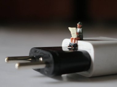 a close up of a miniature figure of a person reading above a cell phone charger.
