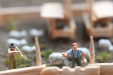 A close up of miniature figure of a goat herder feeding in a wooden cage. Shepherd concept.
