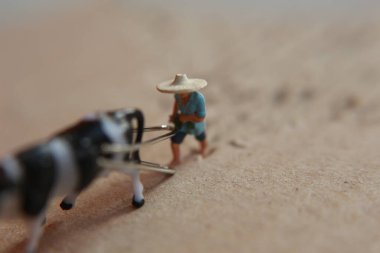 miniature figure of a farmer plowing a field with his cow on a cardboard.