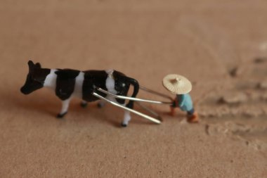 miniature figure of a farmer plowing a field with his cow on a cardboard.