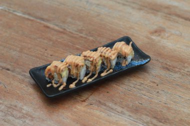 Japanese food called Salmon Mozza Sushi. Served warm on a black rectangular plate on the table.