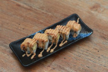 Japanese food called Salmon Mozza Sushi. Served warm on a black rectangular plate on the table.