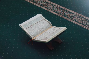 a close up of the holy book Al-Quran on a green prayer rug. Islamic photo concept.