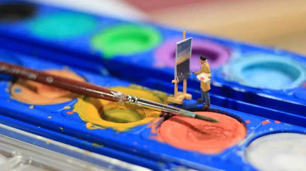a miniature figure of a painter painting a landscape on watercolors. artist concept.