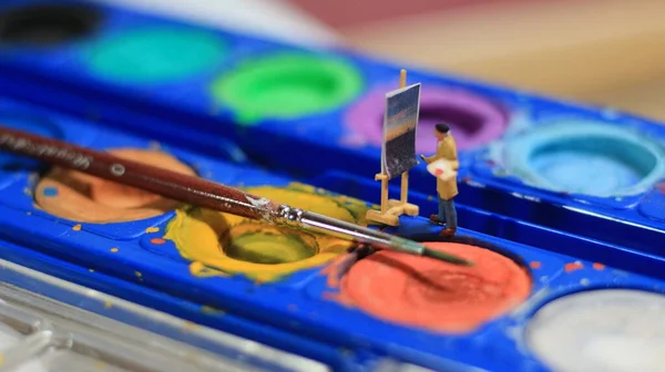 a miniature figure of a painter painting a landscape on watercolors. artist concept.