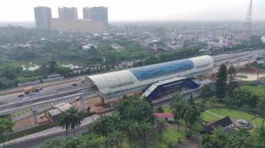 4K footage aerial view of an LRT station under construction, above the expressway and next to a park.