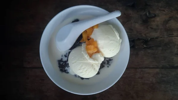 stock image Bubur Ketan Hitam or black sticky rice porridge with added vanilla ice cream and mango pieces. Food concept photo.