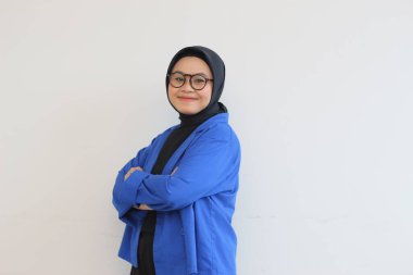 Güzel, Asyalı, genç Müslüman bir kadın. Profesyonel pozda gözlük takıyor ve mavi ceket giyiyor. Sırıtıyor..
