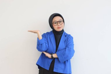 Güzel Asyalı genç Müslüman kadın, gözlüklü ve mavi ceketli yalnız beyaz arka planda gülümserken avuçlarını gösteriyor. reklam kavramı.
