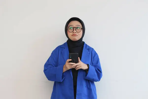 ヒジャーブの美しいアジア系女性の肖像画 携帯電話を白い背景に隔離されたまま青いブレザー思考を身に着けている — ストック写真