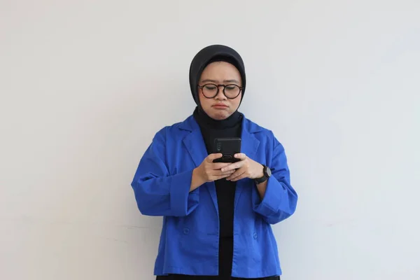 美しいアジア系の若い女性が眼鏡をかけヒジャーブをかけ携帯電話を青いブレザーで見て — ストック写真