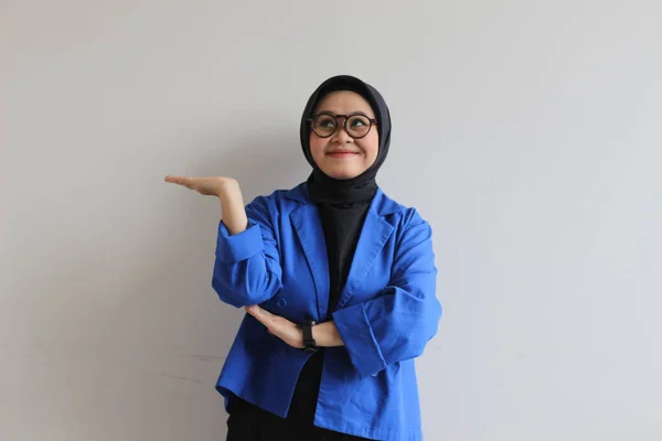 美しい若いアジアのイスラム教徒の女性は 白い背景を笑顔ながらヤシの木を示す眼鏡と青いブレザーを身に着けている 広告コンセプト — ストック写真