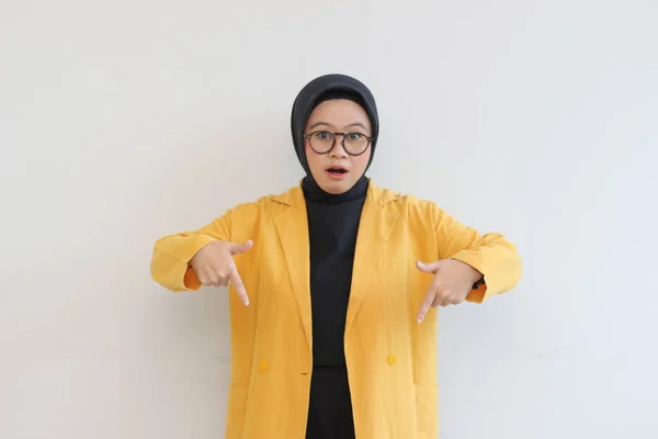 ヒジャーブ 黄色のブレザーを身に着けている美しい若いアジアのイスラム教徒の女性は 白い背景に隔離された下を指して両手でショックを受けた式 広告コンセプト — ストック写真