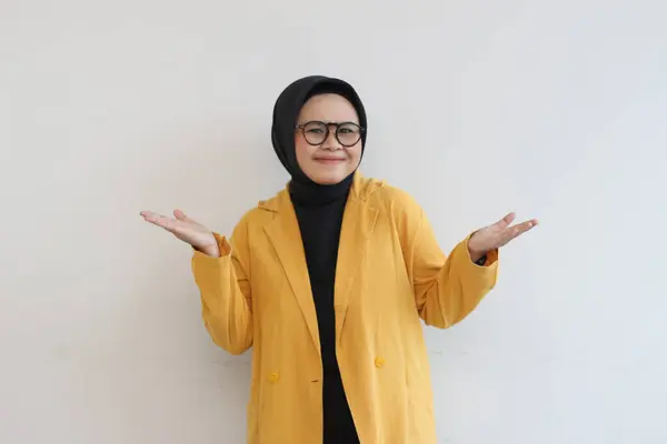 年轻美丽的亚洲穆斯林女子 戴着眼镜 头戴头巾 身穿黄色的夹克 满面春风 满心喜庆 双手空空如也 与白色背景隔离 广告理念 — 图库照片