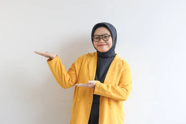 ガラス ヒジャーブ 黄色のブレザーを身に着けている美しい若いアジアのイスラム教徒の女性は自信を持って笑顔と白い背景に隔離された空のスペースを提示両手で幸せ 広告コンセプト — ストック写真