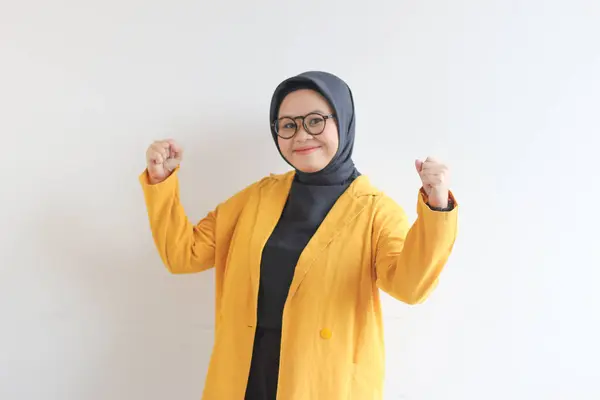 美しい若いアジア系イスラム教徒の女性 彼女の腕と筋肉を持ち上げることによって強いジェスチャーで眼鏡と黄色のブレザーを身に着けています孤立した白い背景 — ストック写真