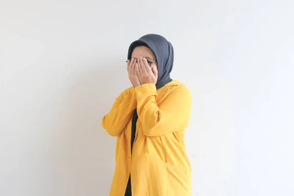 年轻美丽的亚洲穆斯林妇女 戴着眼镜 头戴黄色夹克 双手捂住脸 背景是白色的 — 图库照片