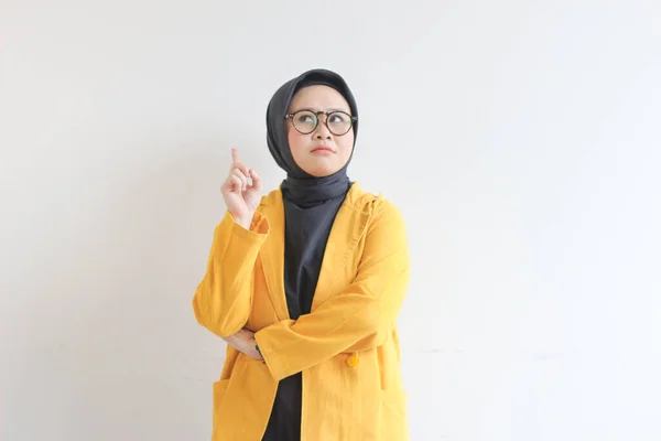 白い背景に隔離された笑顔をしながら 眼鏡と黄色いブレザーを身に着けている美しい若いアジアのイスラム教徒の女性は考えている — ストック写真