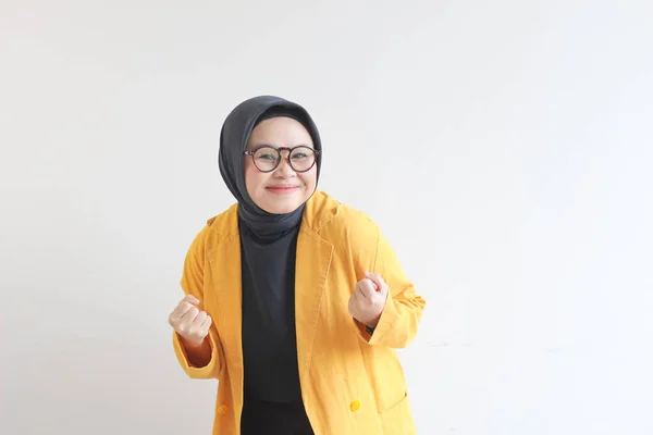 年轻美丽的亚洲穆斯林妇女 戴着眼镜 身穿黄衫 满脸喜色 紧紧抓住拳头 保持白色的背景 — 图库照片