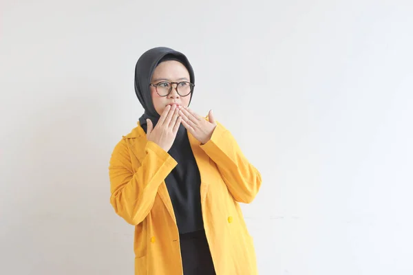 年轻美丽的亚洲穆斯林妇女 戴着眼镜和黄色的夹克 脸上带着震惊的表情 捂着被白色背景隔开的嘴 — 图库照片