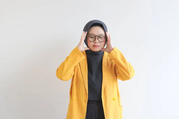 美しい若いアジア系イスラム教徒の女性 眼鏡をかけ 白い背景に隔離された頭を保持めまい式の黄色いブレザーを身に着けています — ストック写真
