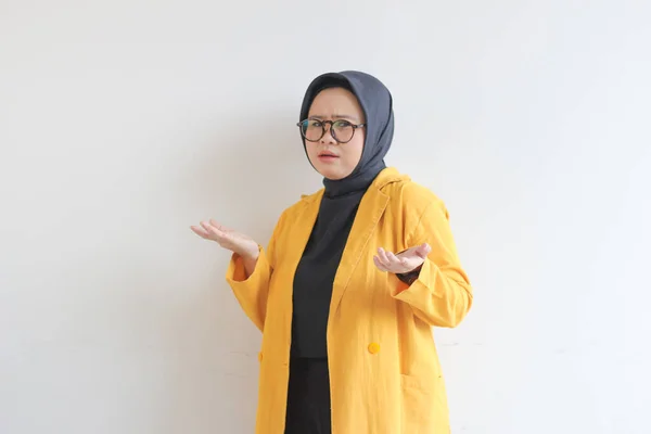 ガラス ヒジャーブ 黄色のブレザーを身に着けている美しい若いアジアのイスラム教徒の女性と混乱した表現と白い背景に隔離された空の空間を提示する手の両方 広告コンセプト — ストック写真