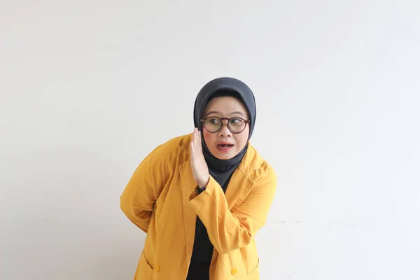 美しい若いアジア系イスラム教徒の女性 ささやきのジェスチャーで眼鏡と黄色のブレザーを身に着けています — ストック写真