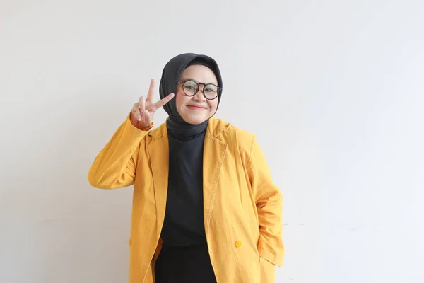 年轻美丽的亚洲穆斯林妇女 戴着眼镜 身穿黄色夹克 象征和平 与白色背景隔离 — 图库照片