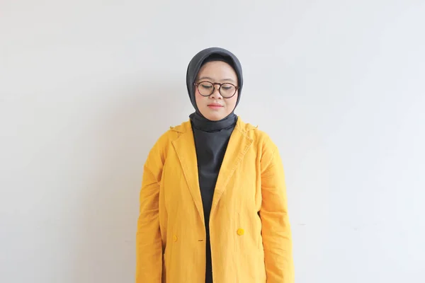 若い美しいアジア系イスラム教徒の女性 眼鏡と黄色のブレザーを身に着けていることは白の背景に隔離された何かを見下ろして笑って — ストック写真