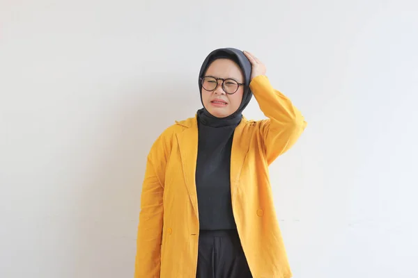 白い背景に隔離された頭を保持しながら ストレスジェスチャーを示す眼鏡と黄色のブレザーを身に着けている美しい若いアジアのイスラム教徒の女性 広告コンセプト — ストック写真