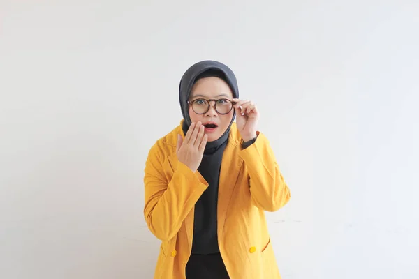 年轻美丽的亚洲穆斯林妇女 身穿黄色夹克 看着镜头 手里拿着一副白色背景的眼镜 很奇怪 — 图库照片