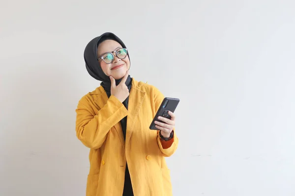 白を基調とした携帯電話を持ちながらも ヒジャーブ 黄色いブレザー思考で美しいアジアの女性の肖像画 — ストック写真