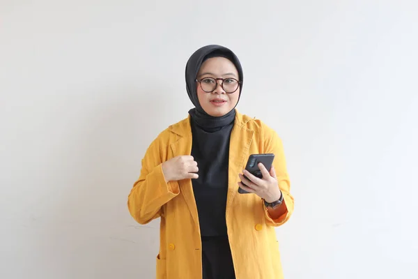 年轻美丽的亚洲女人戴着眼镜 头戴头巾 头戴黄色的夹克 手里拿着一部笔直的手机 脸与白色背景隔离 — 图库照片