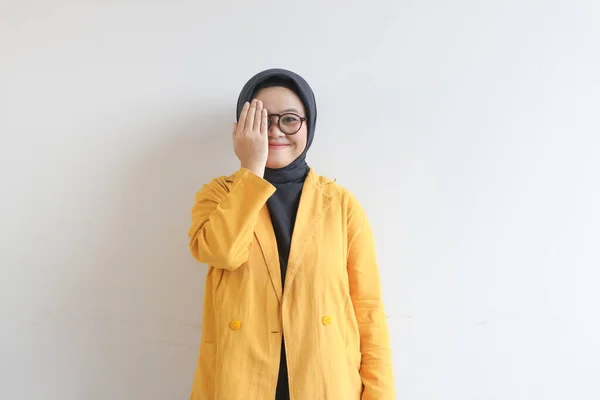 年轻美丽的亚洲穆斯林妇女 戴着眼镜 头戴黄色的夹克 手捂住脸的一侧 面带白色背景 面带微笑 — 图库照片