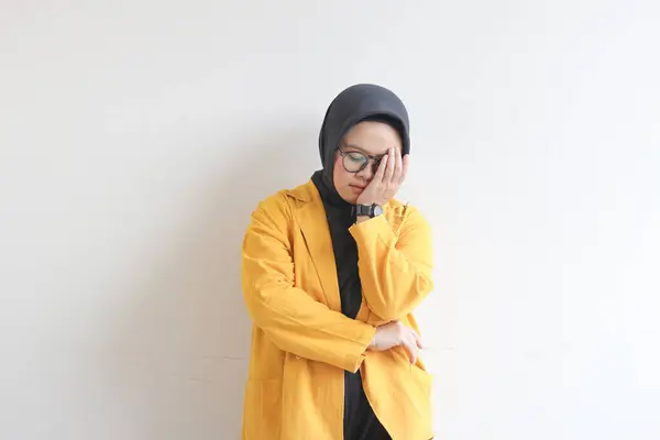 年轻美丽的亚洲穆斯林妇女 戴着眼镜 头戴黄色的夹克 手被白色的背景隔开 遮住了脸的一侧 — 图库照片
