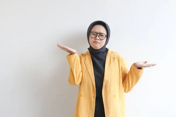 年轻美丽的亚洲穆斯林妇女 戴着眼镜 身穿黄色夹克 脸上困惑的表情与白色背景隔离 — 图库照片